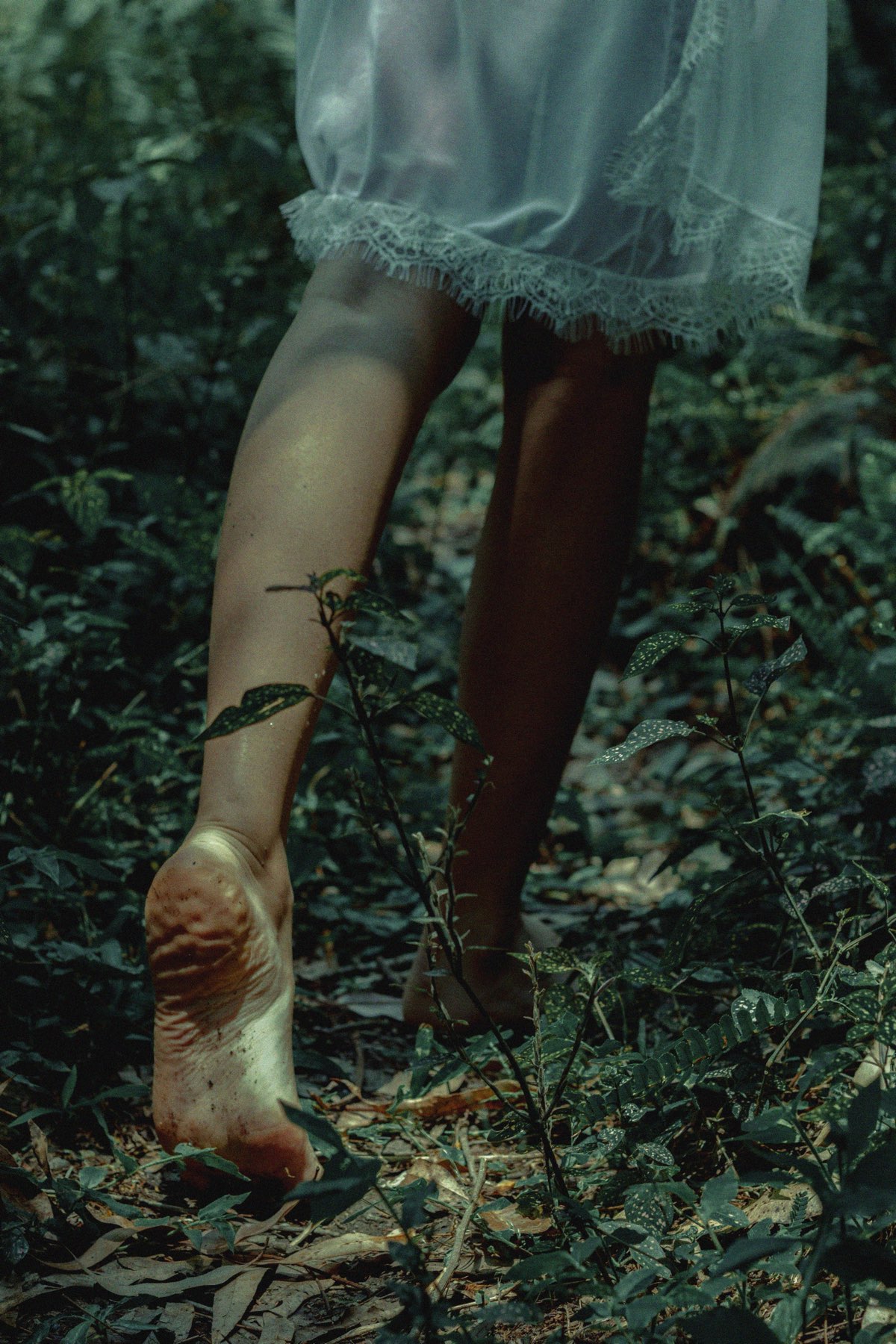A barefoot figure walking forward through a forest path